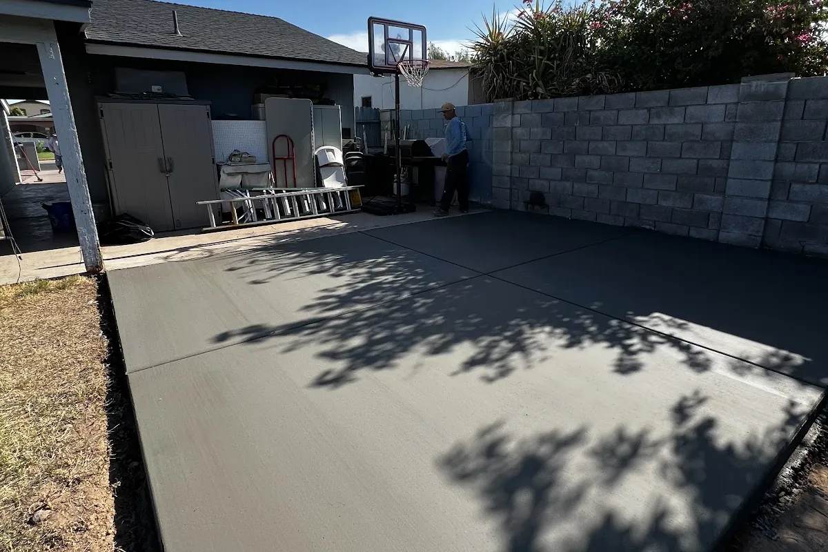 A new broom-finished backyard concrete pad beside a block wall, poured by our featured contractor