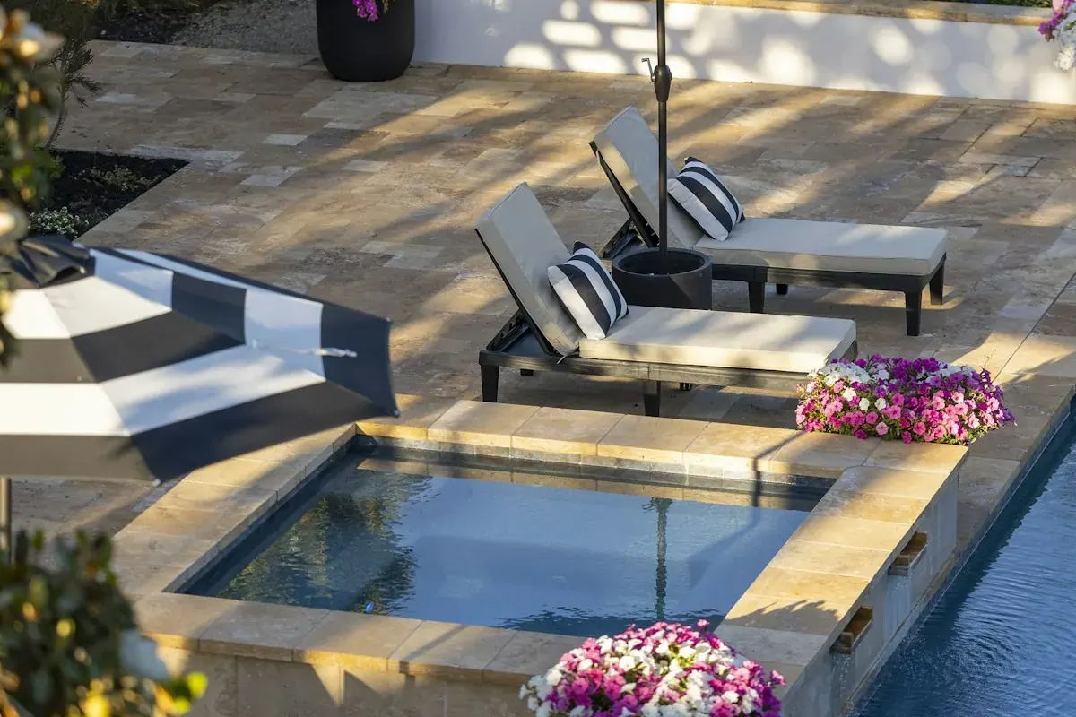A spa set into a patio with lounge chairs and potted flowers